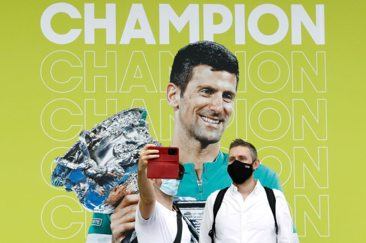 Spectators pose for a selfie with a banner of 2021 Men's Australian Open winner Novak Djokovic