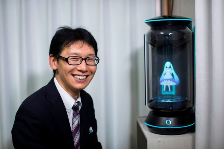 Japanese Akihiko Kondo poses next to a hologram of Japanese virtual reality singer Hatsune Miku