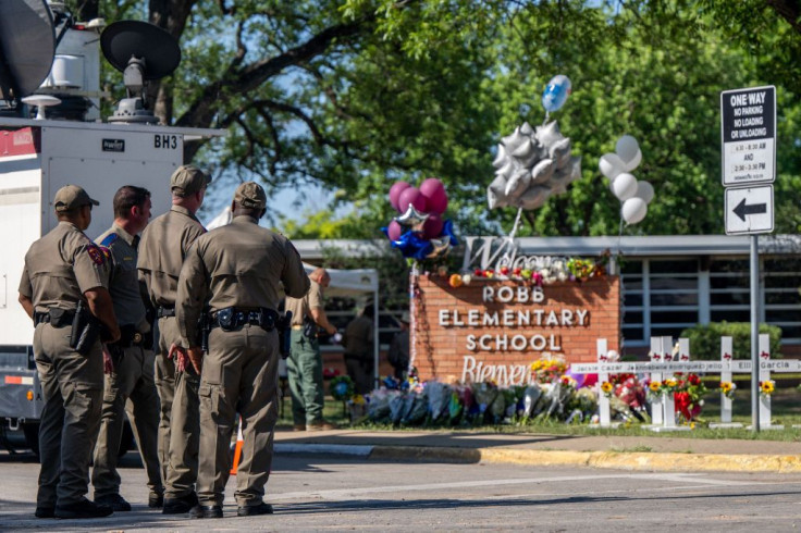 Law enforcement officers stand looking at a memorial following a mass shooting at Robb Elementary School