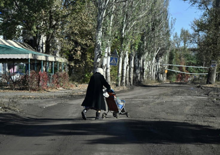 An elderly woman carries bottles of water in a child