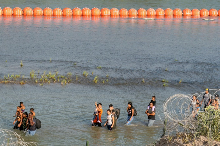 Migrants walk between concertina wire and a string of buoys placed on the water along the Rio Grande river with Mexico in Eagle Pass, Texas