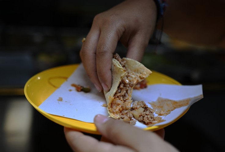 A woman eats a taco at a street food stall